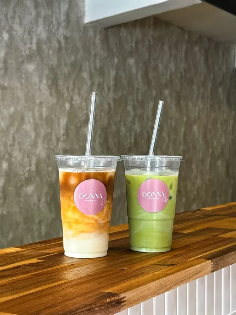 Un latte glacé et un matcha glacé dans des gobelets Donna, sur le comptoir en bois du café
